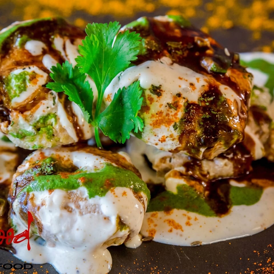 Plated Indian chaat dumplings topped with yogurt, green chutney, tamarind sauce, spices, and fresh cilantro.