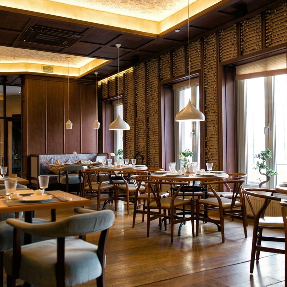 Elegant restaurant dining room with set wooden tables, pendant lights, large windows, and textured walls lined with wine corks.