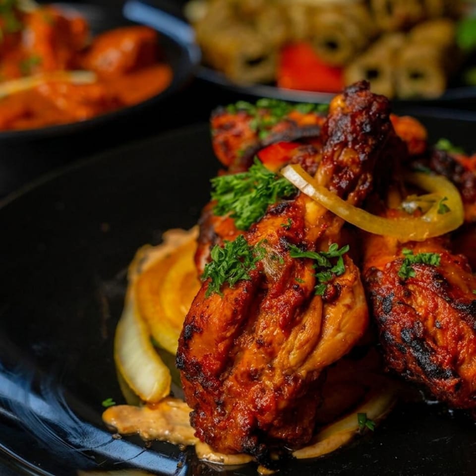 Grilled spiced chicken skewers garnished with parsley and onions on a black plate, with colorful side dishes in the background.